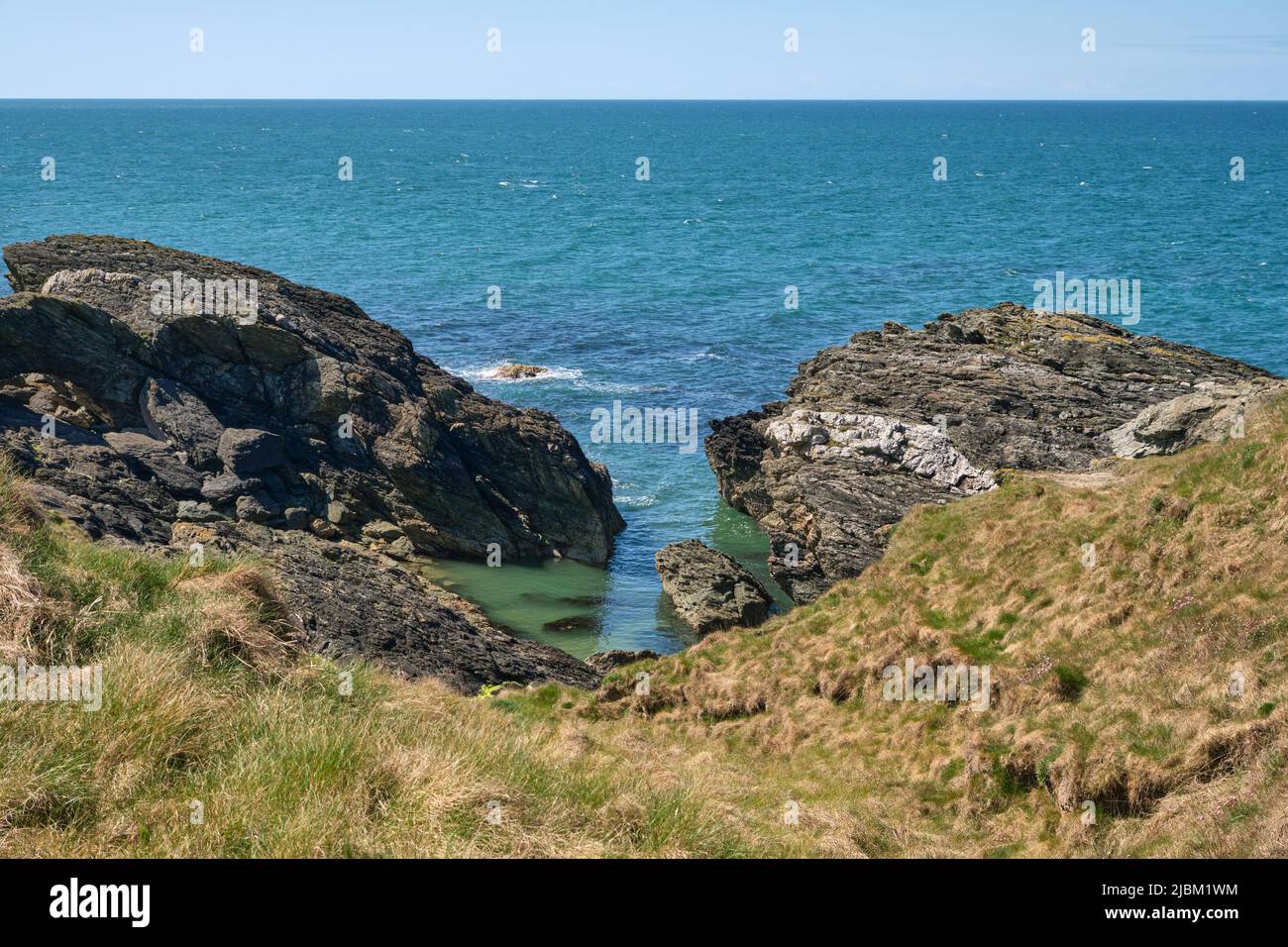 A small cove of green water along the rugged northern coast of the Llyn Peninsula on the Wales Coast Path Stock Photo