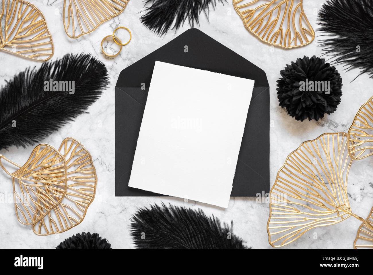 Blank card and black envelope on marble table near black feathers and ...