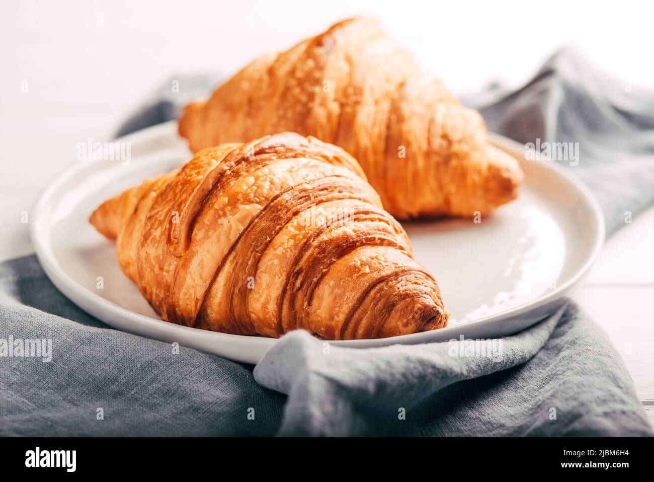 Plate with two fresh croissants on white table. Stock Photo
