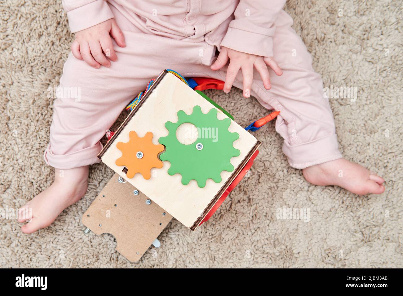 Happy toddler baby boy is playing with a busyboard cube on the nursery floor. Educational toys for children, wooden game panel. A child aged one year Stock Photo