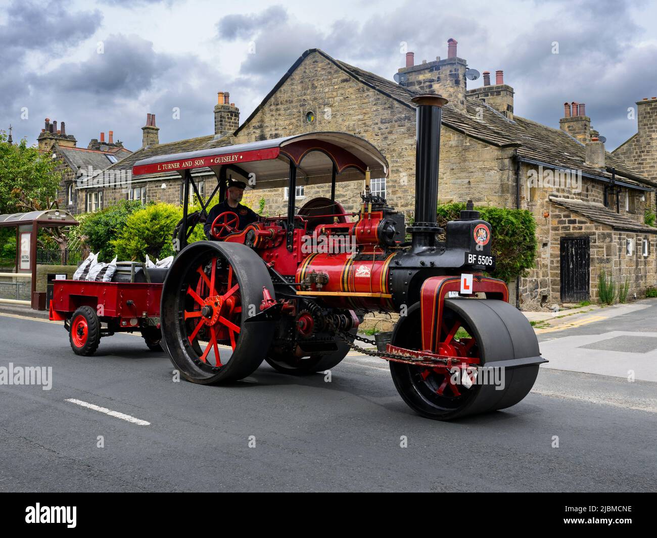 Vintage restored heavy old-fashioned red steam-powered vehicle (black chimney, L-plate, driver) - Burley-in-Wharfedale, West Yorkshire, England, UK. Stock Photo
