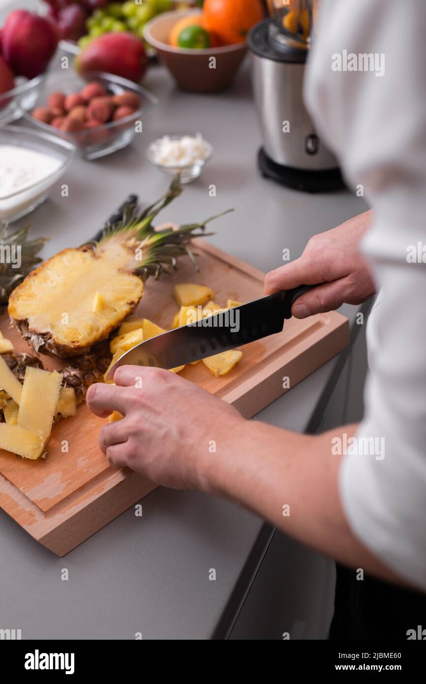 Unrecognizable man cutting a pineapple on chopping board. Stock Photo