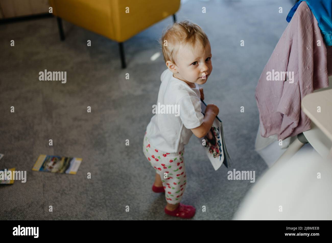 Cute little girl holding book in living room at home Stock Photo - Alamy