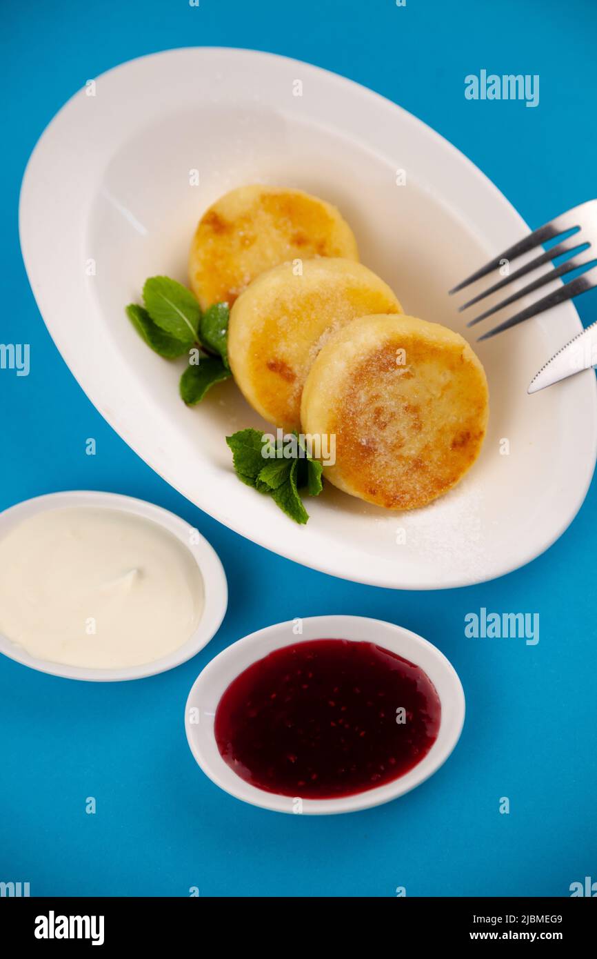 A portion of three round curd cheese pancakes on a white plate. Healthy breakfast. Blue background. Copy space. Stock Photo