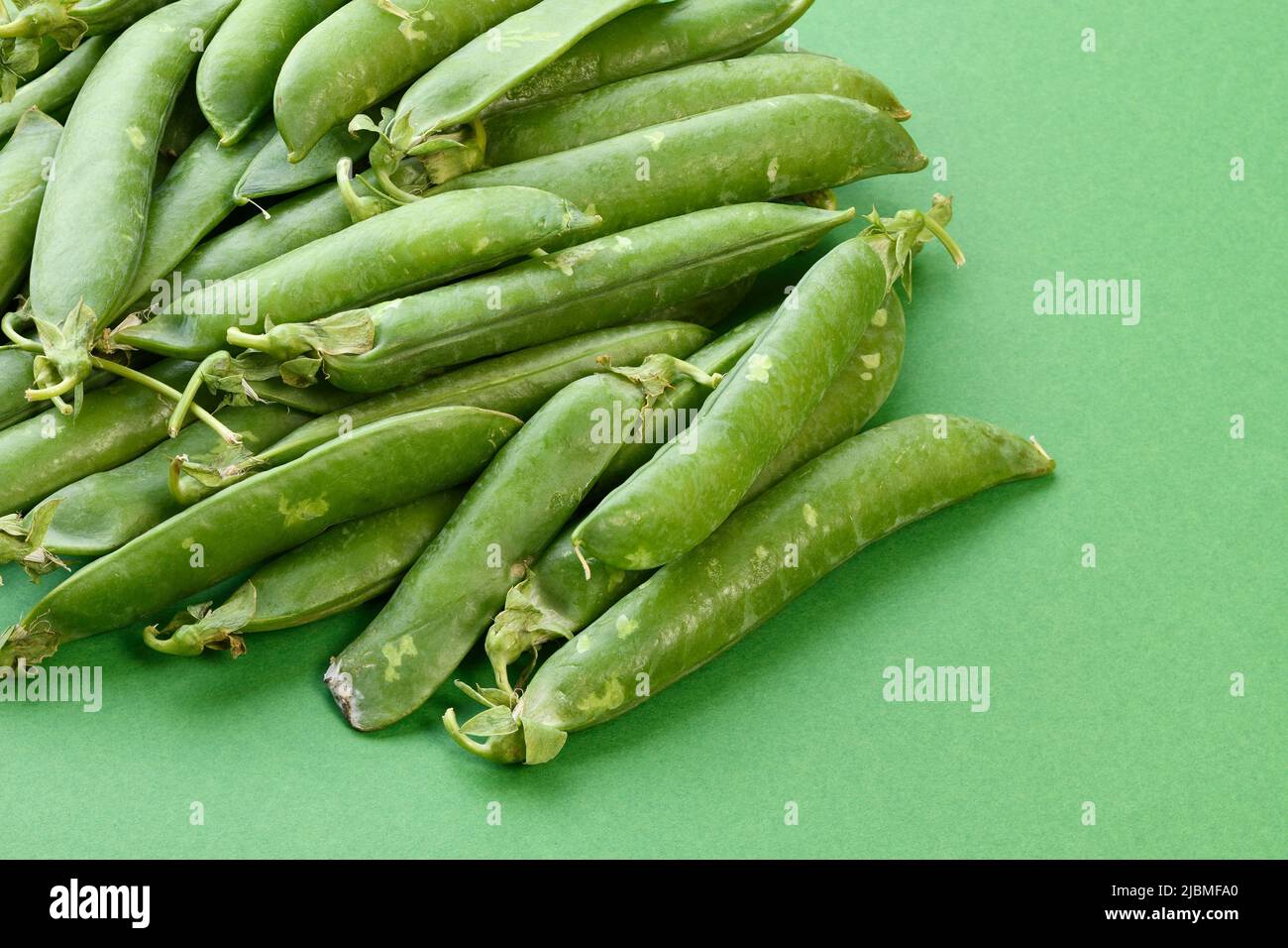 A pile of peas in pods on a green background Stock Photo