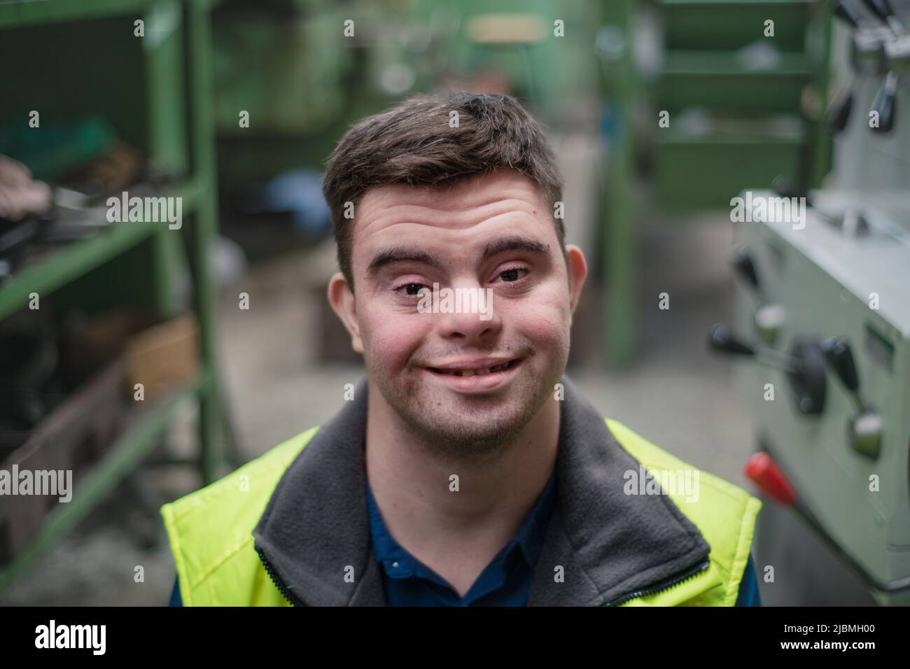 Young man with Down syndrome working in industrial factory, social integration concept. Stock Photo