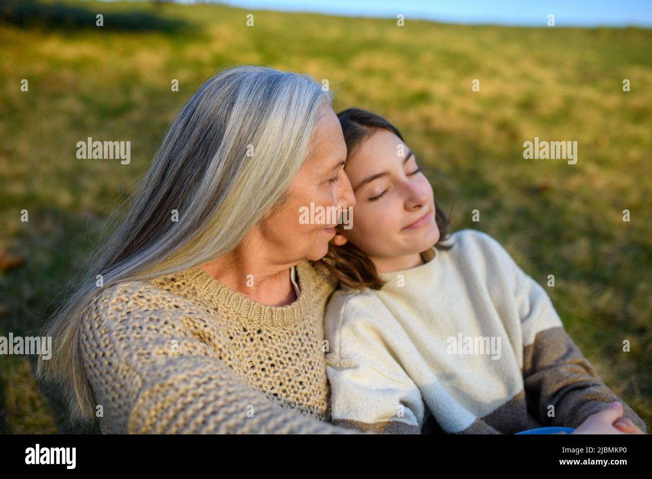 Happy senior grandmother with teenage granddaguhter hugging in nature on spring day. Stock Photo