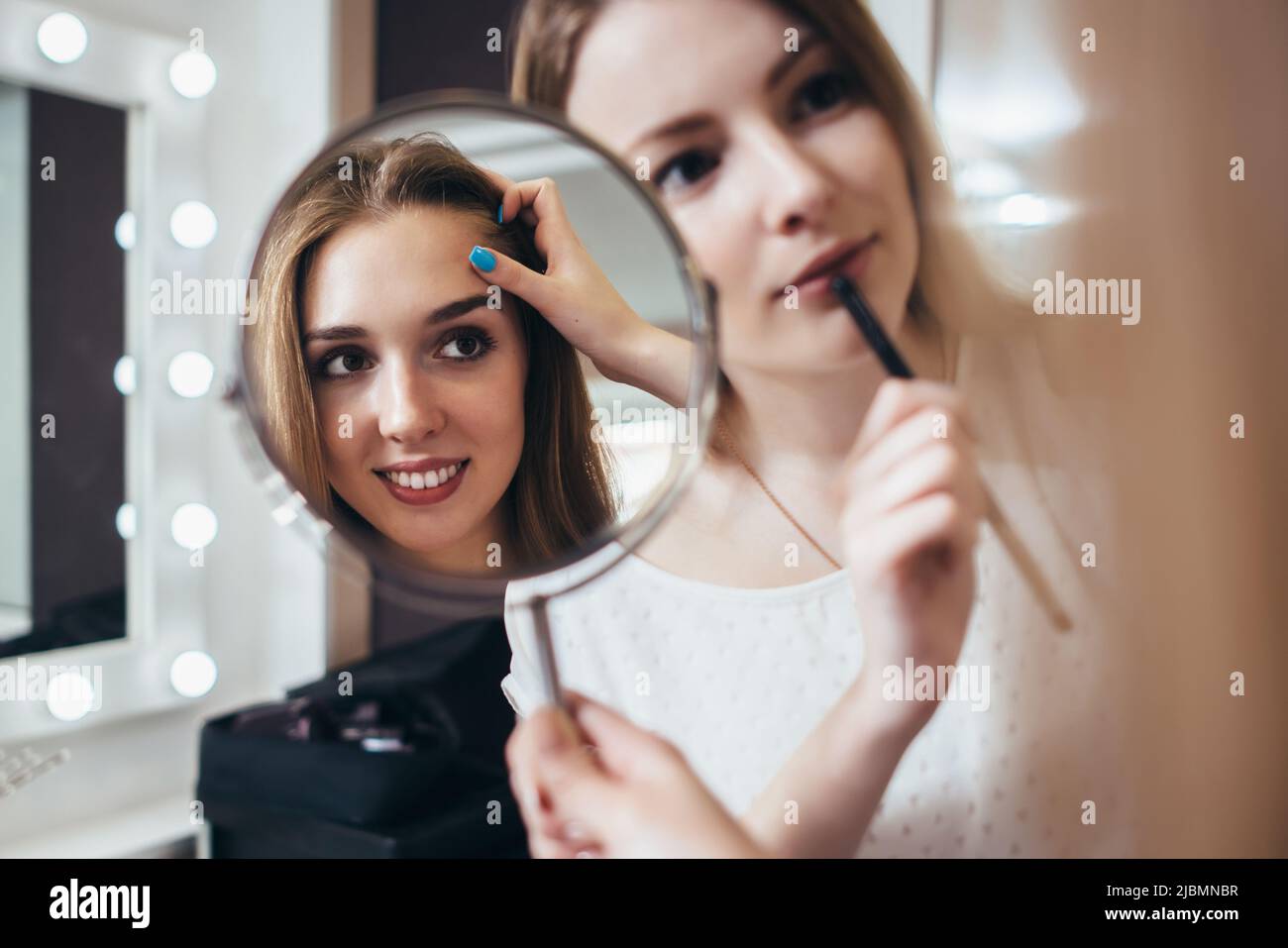 Young female client looking in the mirror while makeup artist working