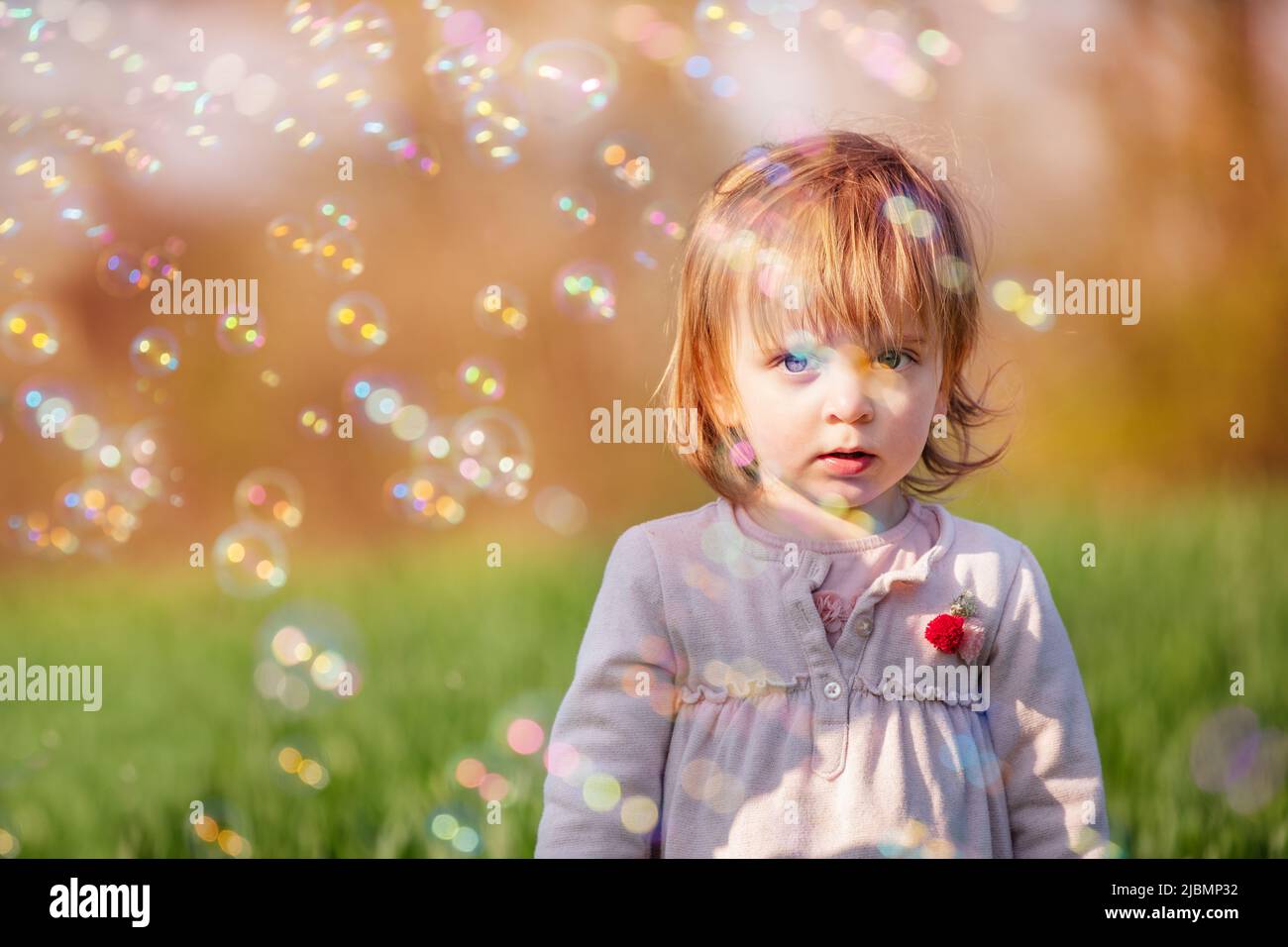 Little smiling baby girl play with soap bubbles in green field Stock Photo