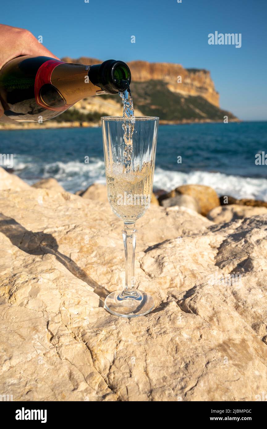 Pouring of French champagne sparkling wine in glass and view on beach