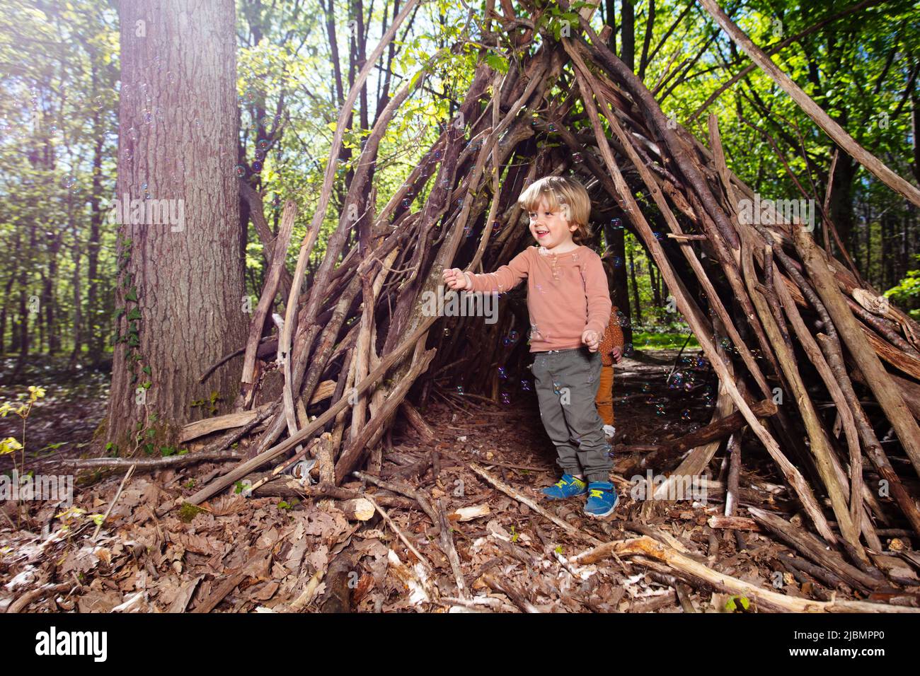 Blond boy play with soap bubbles in forest hut of branches Stock Photo