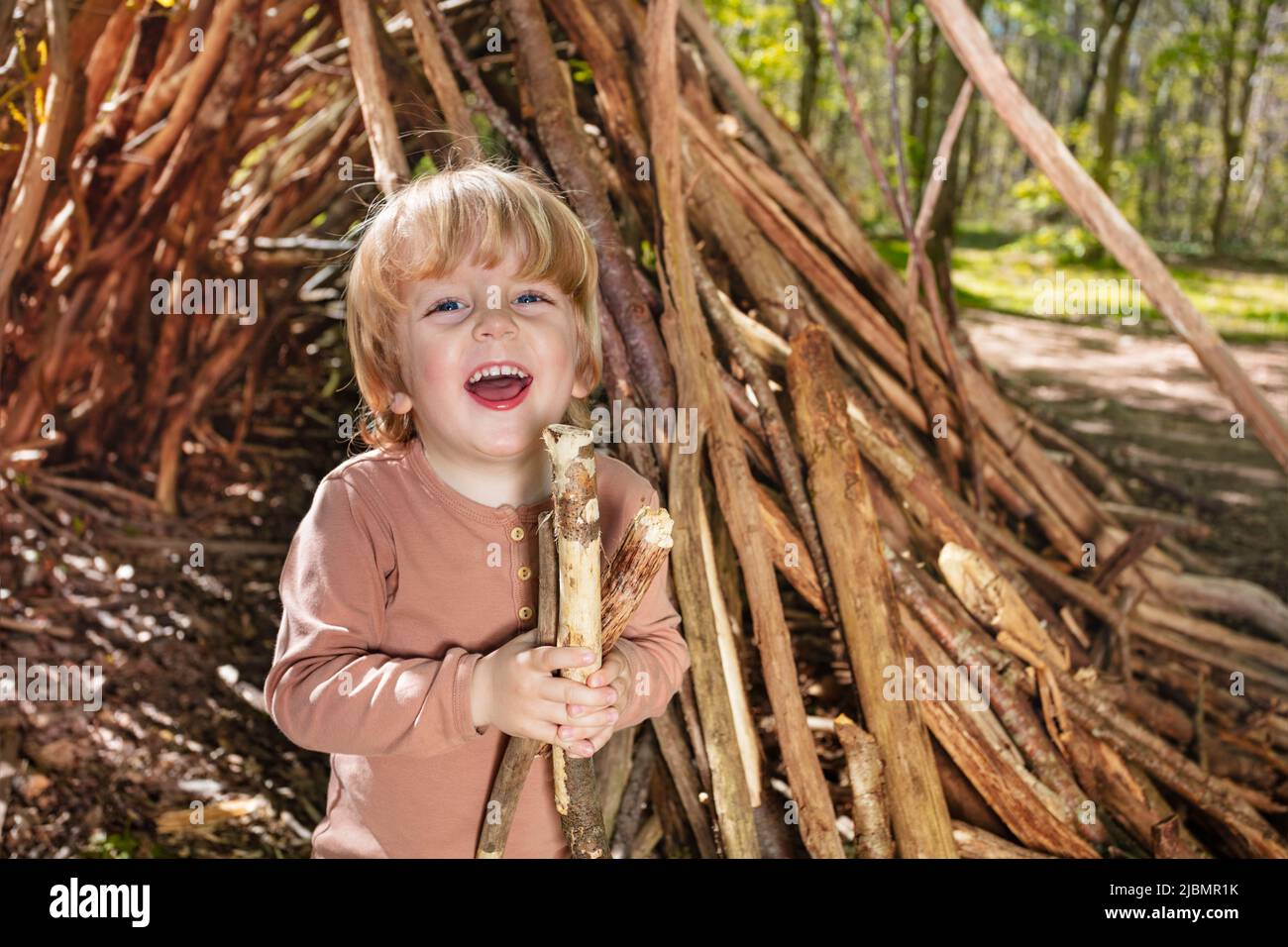 Boy play with brushwood in forest hut of branches, laughing Stock Photo