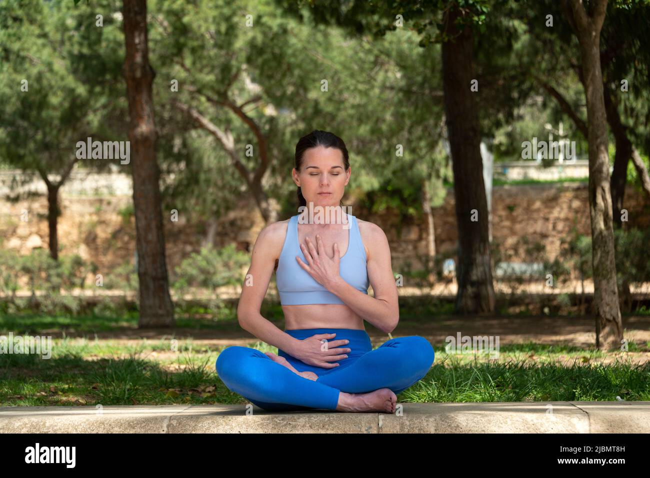 Sporty woman sitting in the park with her legs crossed practicing yoga and meditating. Stock Photo