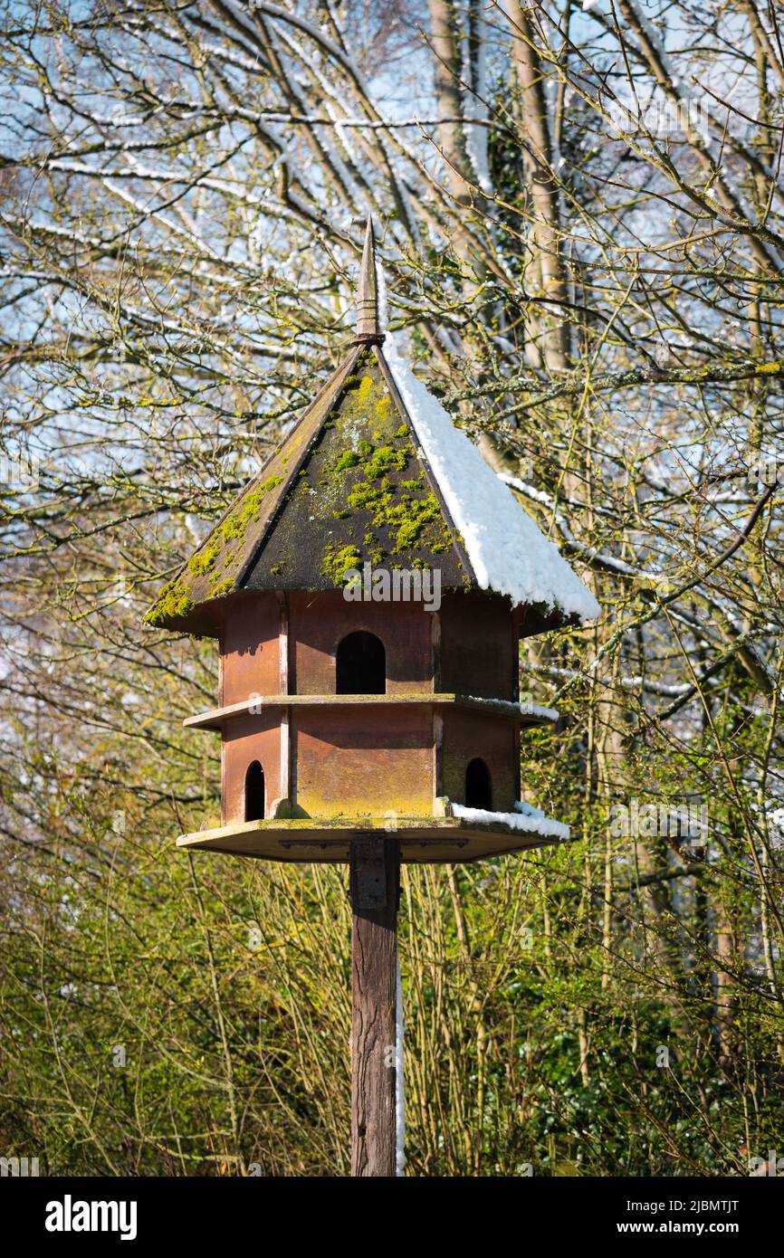 Hexagonal wooden bird house and feeder with Spring snow in bright sunshine Stock Photo