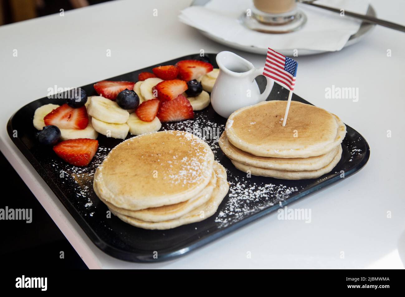 Pancakes and fruit and cream served on a rectangular tray with a miniature American flag inserted into the pancakes. Stock Photo