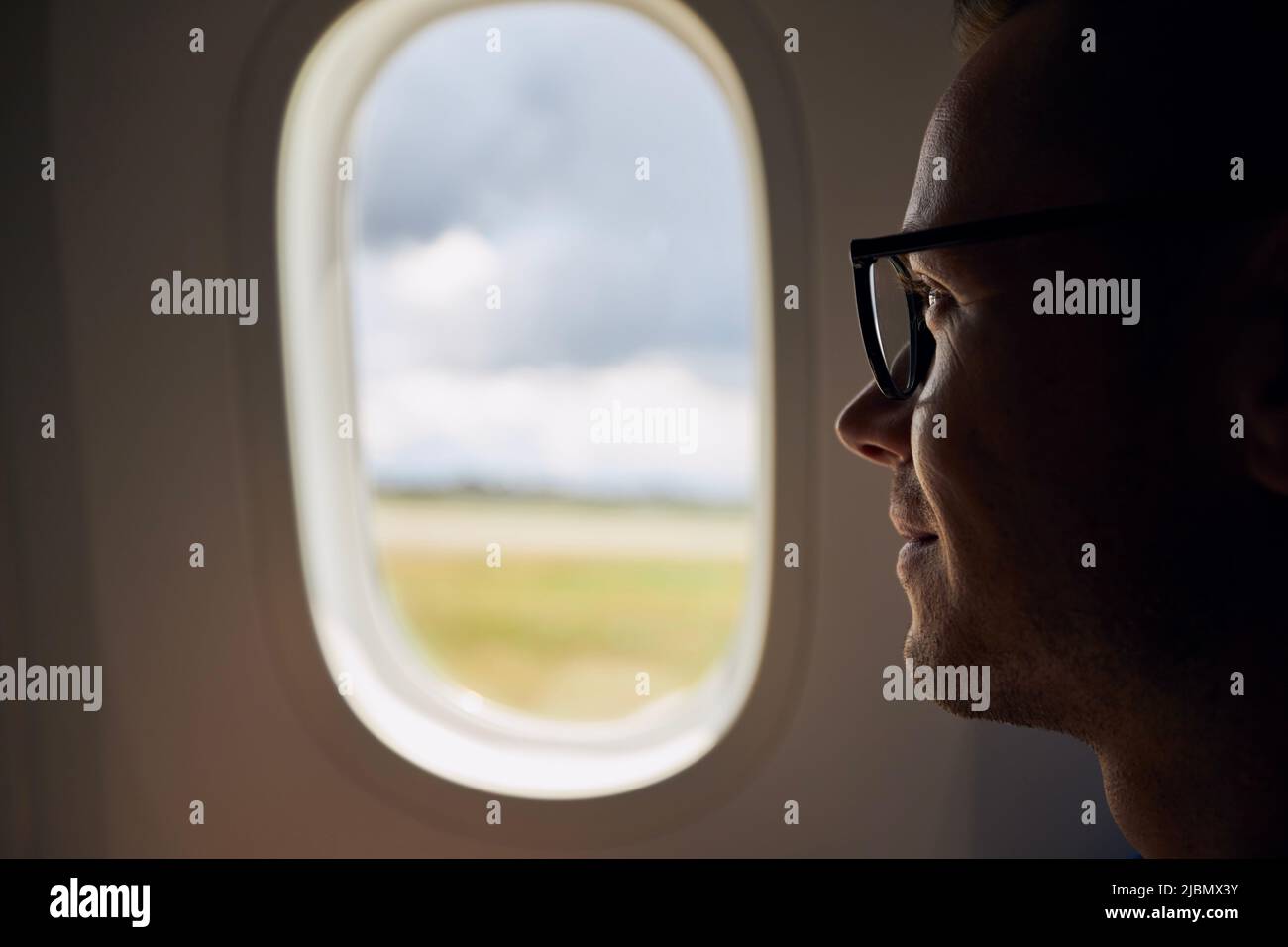 Portrait of man traveling by airplane. Passenger looking through plane window during taxiing at airport. Stock Photo