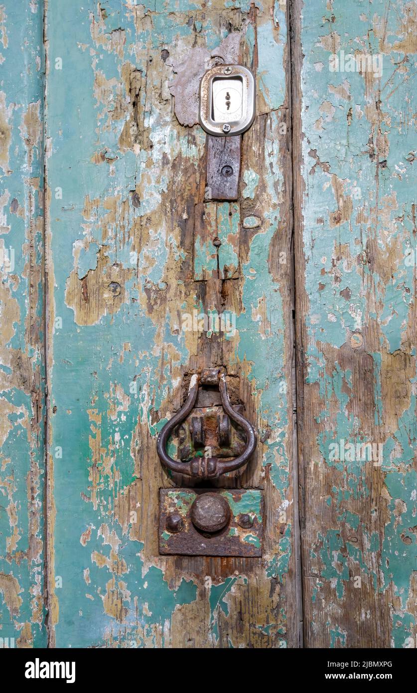 Old dilapidated wooden door, with iron door knocker and green peeling paint Stock Photo