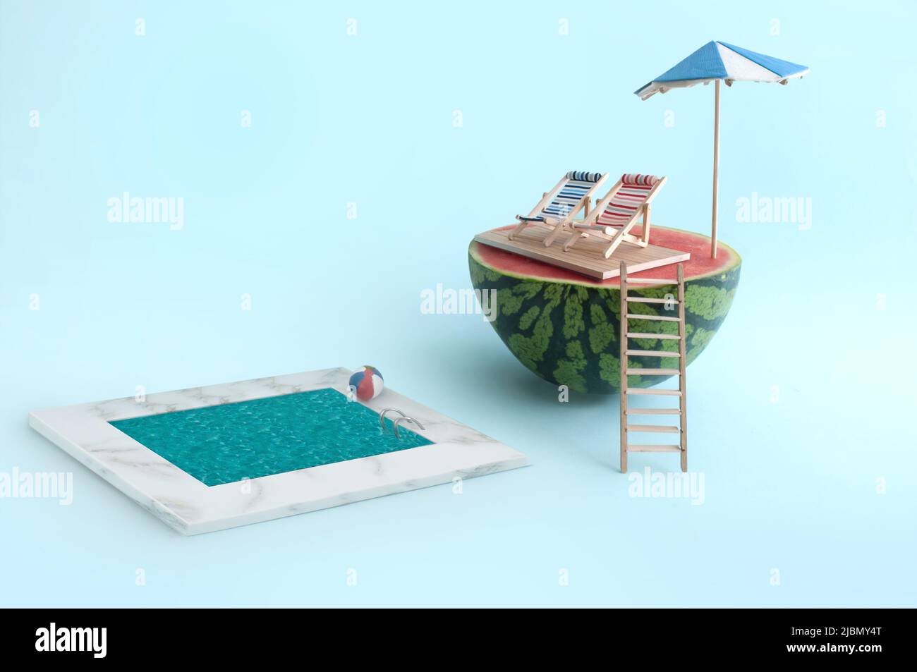 Summer beach holiday concept, watermelon with parasol and two deck chairs near to a swimming pool Stock Photo