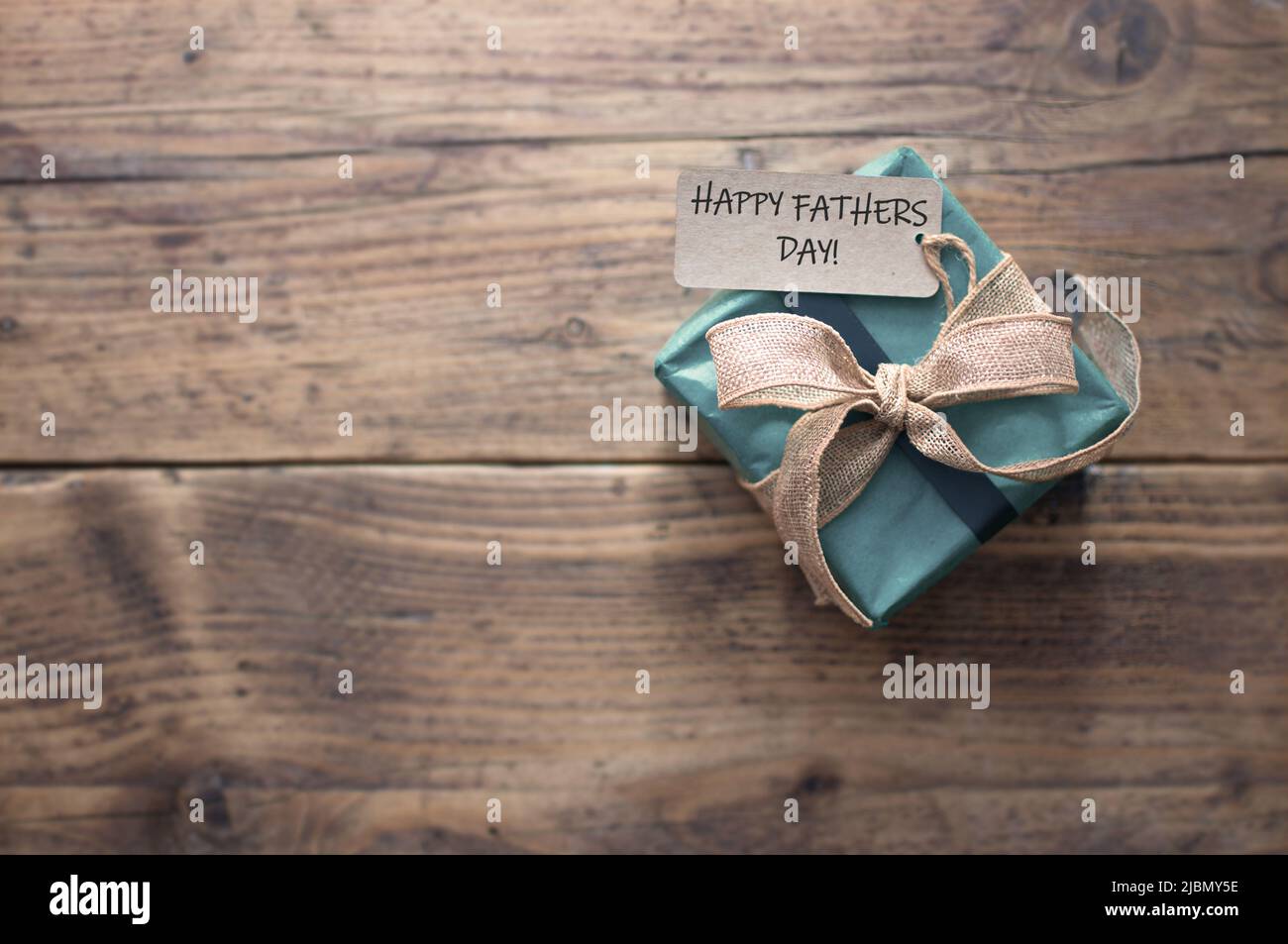 Fathers day greeting attached to gift box wrapped with a rustic ribbon bow on an old wooden table Stock Photo