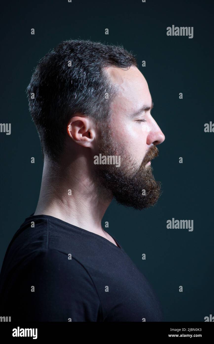 dramatic portrait profile of millennial bearded guy on black background Stock Photo