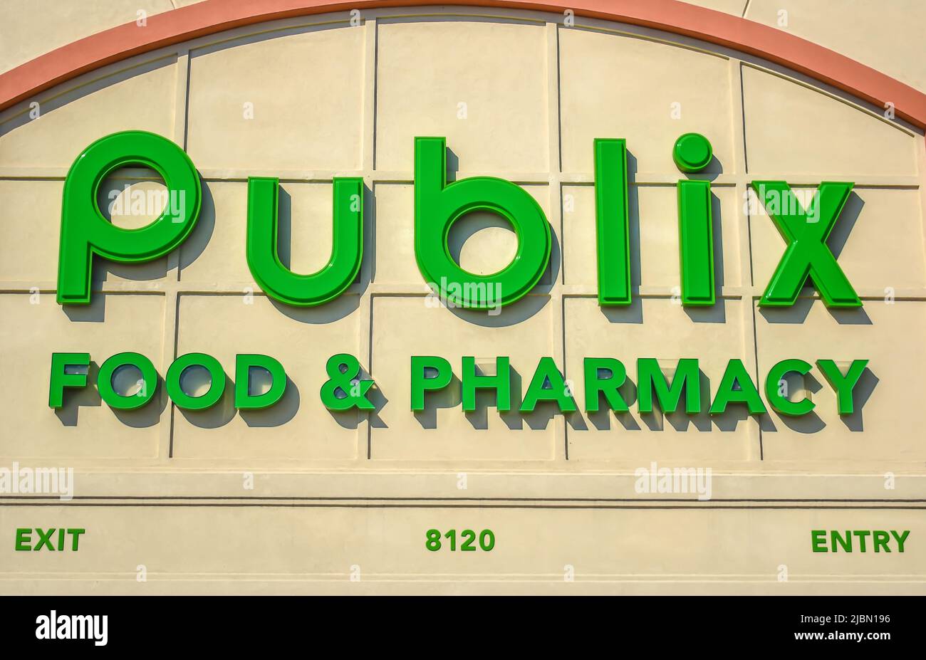 Publix Food & Pharmacy grocery market's exterior facade brand and logo signage in neon green letters on beige in sunset light on a sunny day. Stock Photo