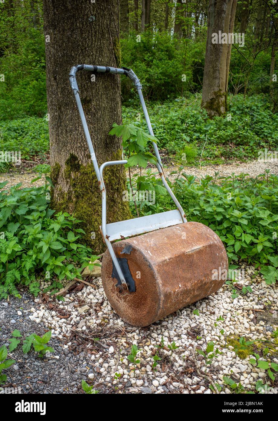 Old rusty garden roller leaning up against a tree in a wooded area. Stock Photo