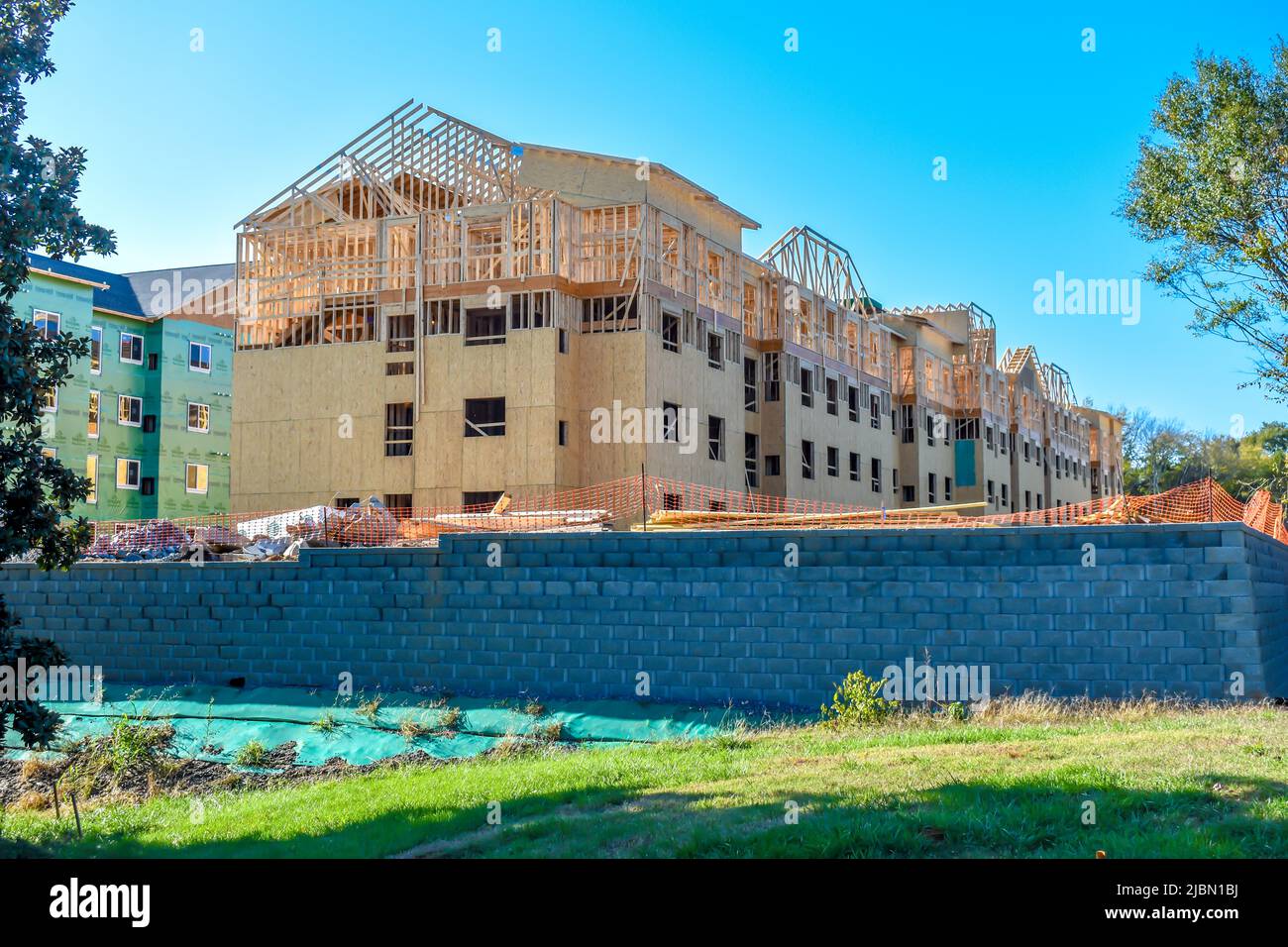 New housing under construction on a bright sunny day with a clear blue sky green tree leaves, grass and a stone retaining wall. Stock Photo