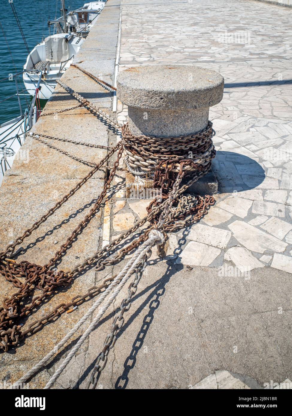 A concrete capstan on a stone quayside with chains and ropes attached on a sunny day. Stock Photo