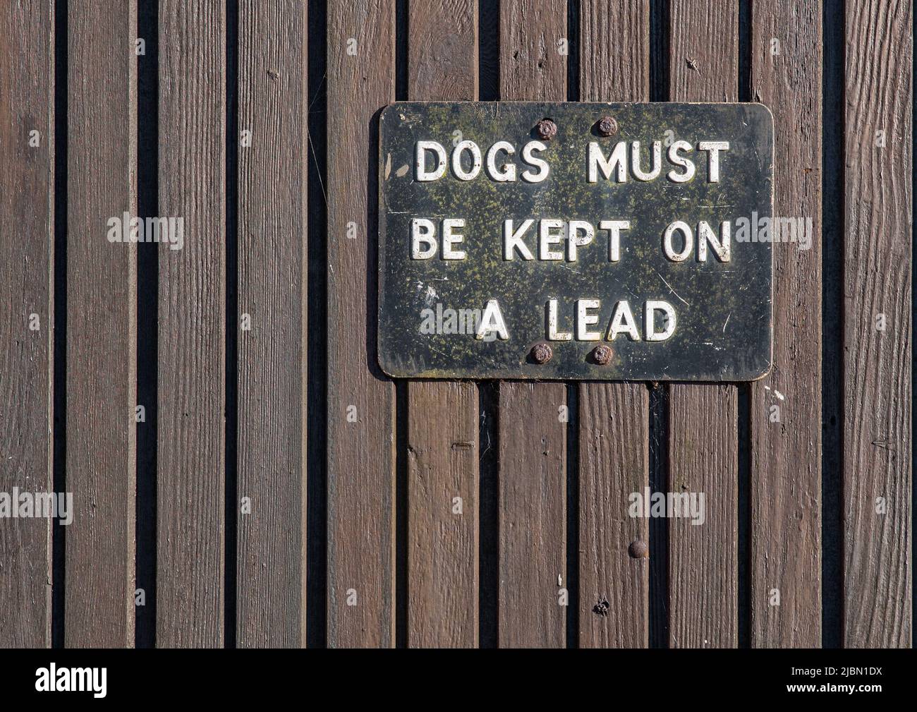 Black and white metal sign on a wooden wall saying dogs must be kept on a lead. Stock Photo