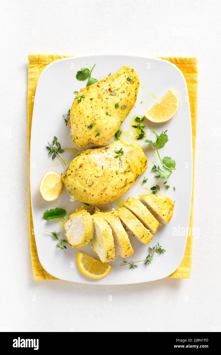 Baked turmeric chicken breast on plate over white stone background. Top