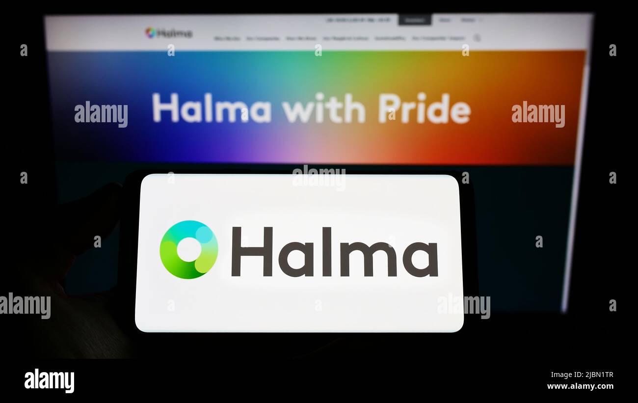Person holding smartphone with logo of British safety equipment company Halma plc on screen in front of website. Focus on phone display. Stock Photo