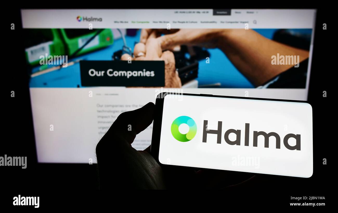 Person holding cellphone with logo of British safety equipment company Halma plc on screen in front of business webpage. Focus on phone display. Stock Photo