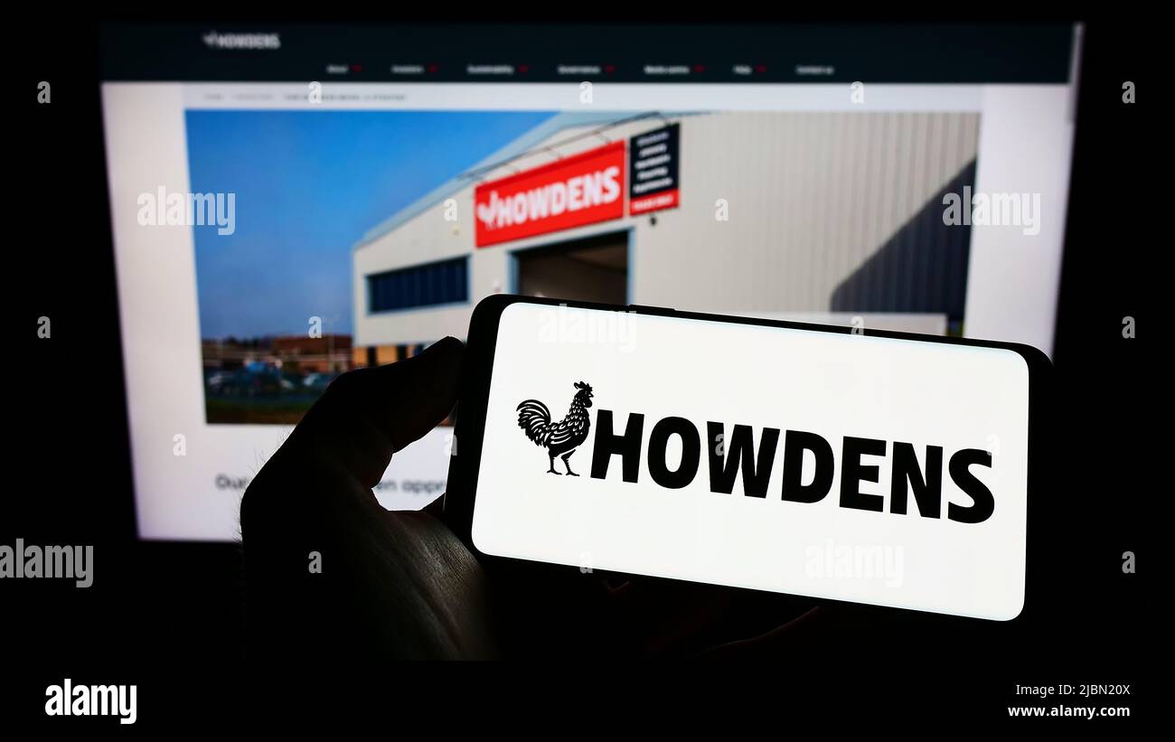 Person holding cellphone with logo of British company Howden Joinery Group plc on screen in front of business webpage. Focus on phone display. Stock Photo