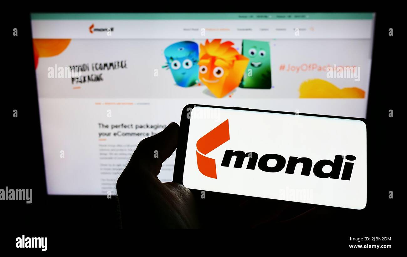 Person holding mobile phone with logo of packaging company Mondi plc on screen in front of business web page. Focus on phone display. Stock Photo