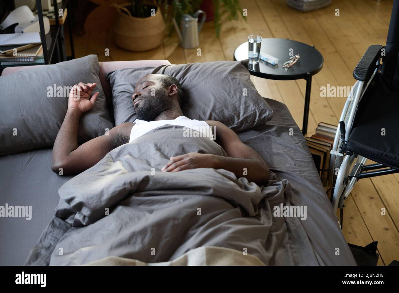 African American man lying on bed under blanket and resting because feeling himself bad Stock Photo