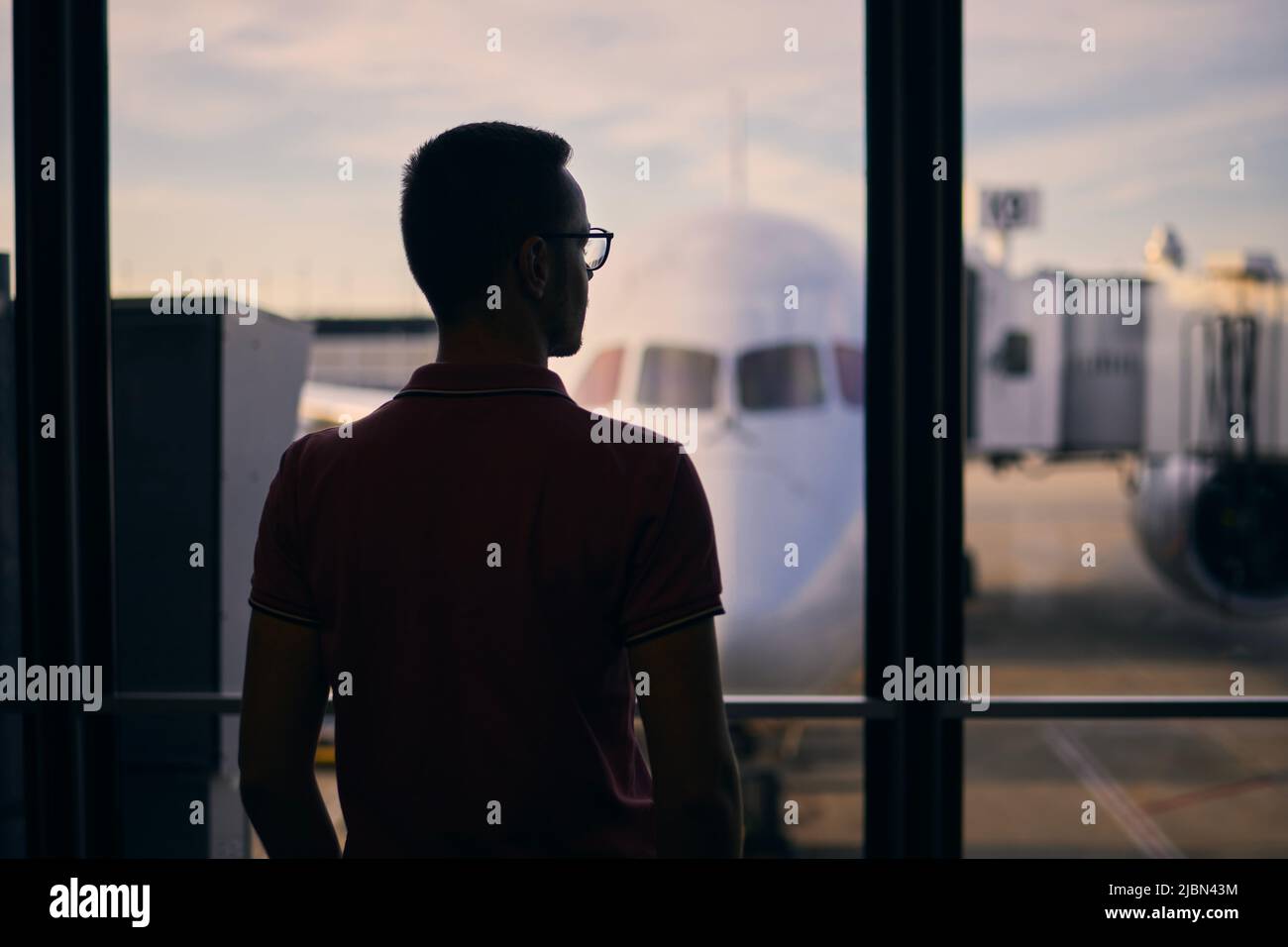 Silhouette of man while waiting for flight. Traveler looking from window of airport terminal before boarding to airplane. Stock Photo