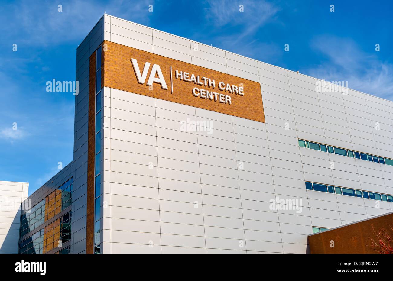 VA Health Care Center's exterior facade brand and logo signage on a bright sunny day with blue sky, hazy clouds, floors and windows. Stock Photo