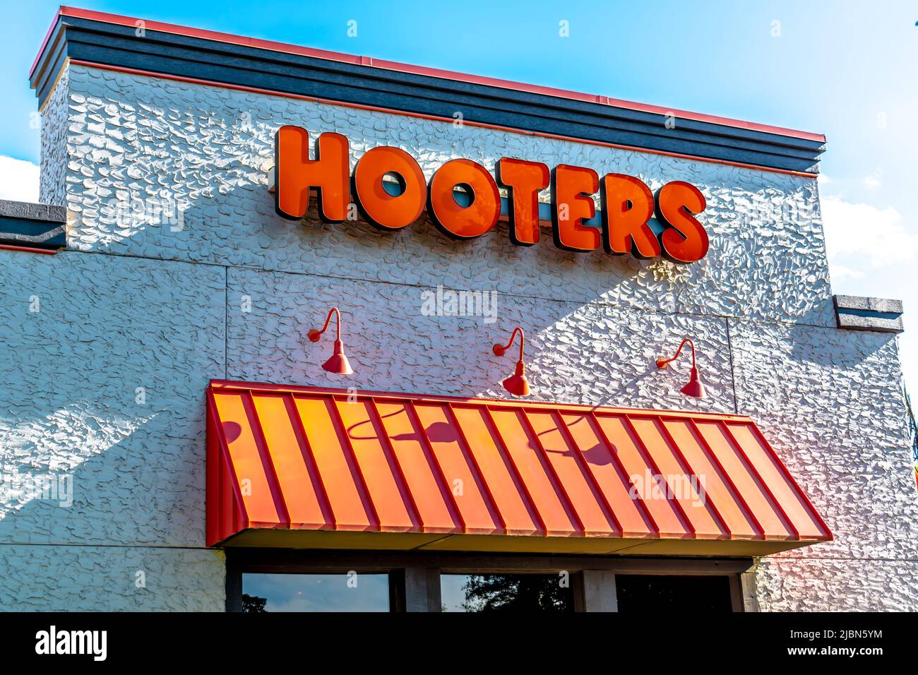 Hooters outdoor facade brand and logo signage in bold, orange letters above a ribbed, metal awning, on a textured building in bright sunlight. Stock Photo
