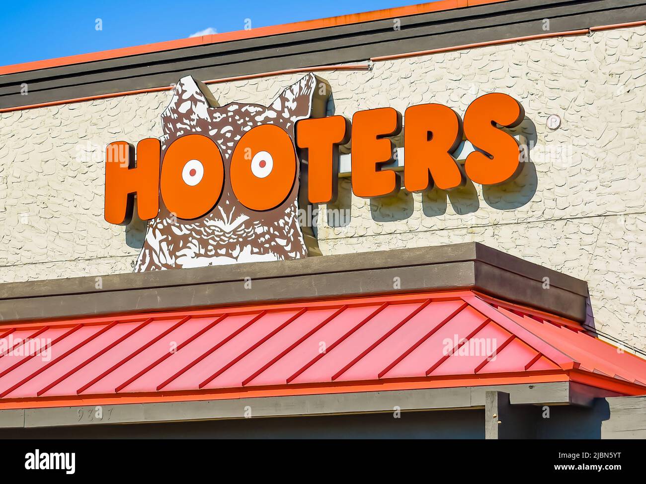 Hooters outdoor facade brand and logo signage in bold, orange letters above a ribbed, metal awning, on a textured building in bright sunlight. Stock Photo