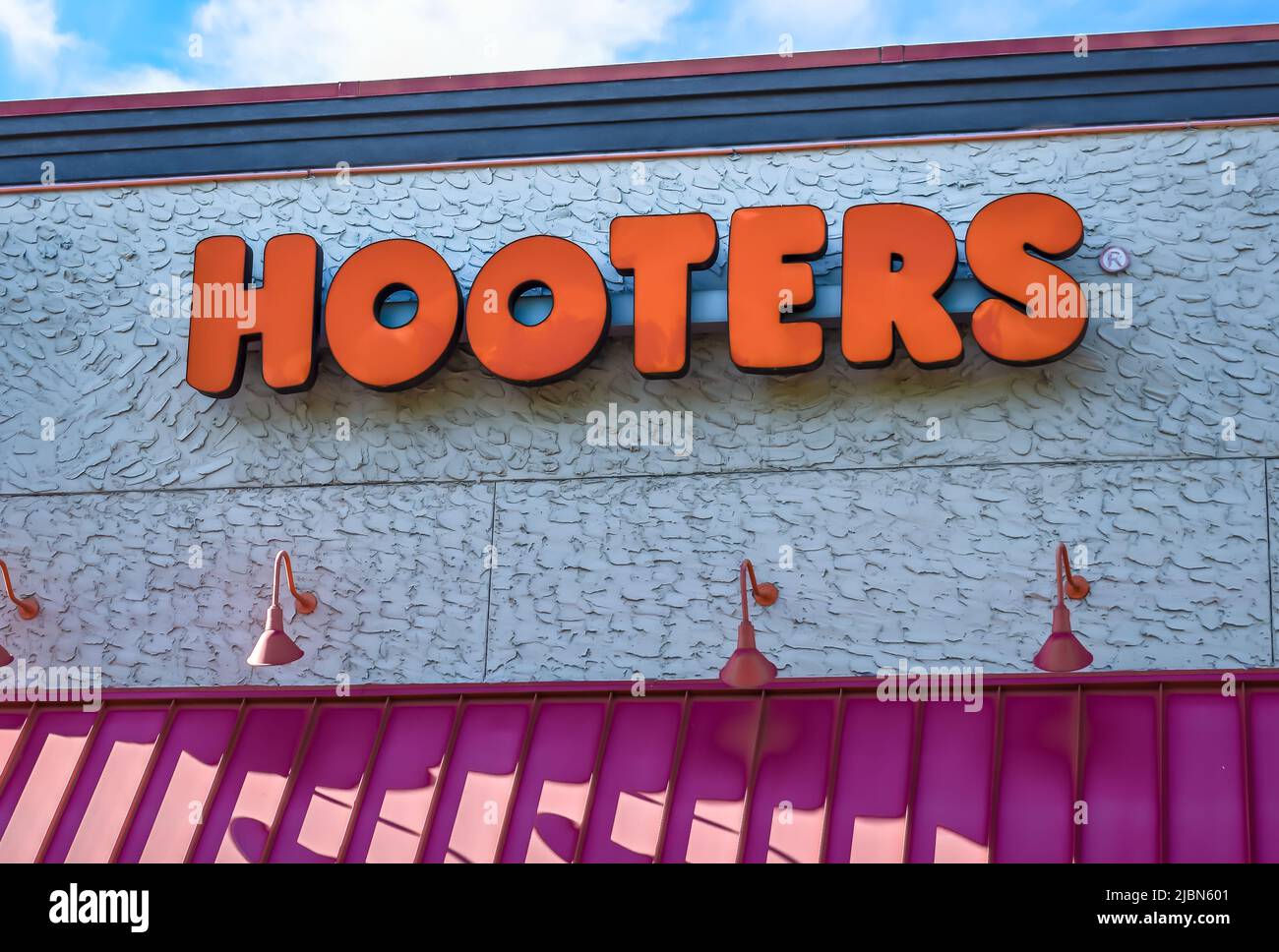 Hooters outdoor facade brand and logo signage in bold, orange letters above a ribbed, metal awning, on a textured building in bright sunlight. Stock Photo