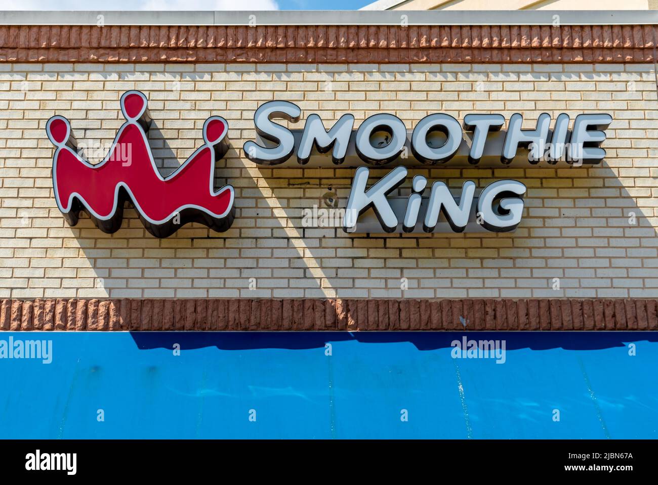 Smoothie King's exterior facade brand and logo signage in white three dimensional letters on beige brick above brilliant blue awning in sunshine. Stock Photo