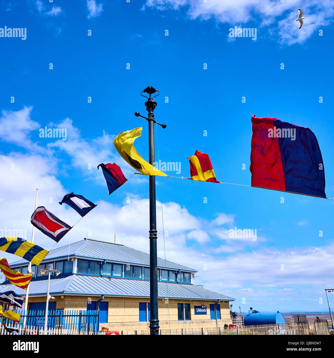 Assorted flags blowing in the wind over Fleetwood ferry terminal and the lifeboat station Stock Photo
