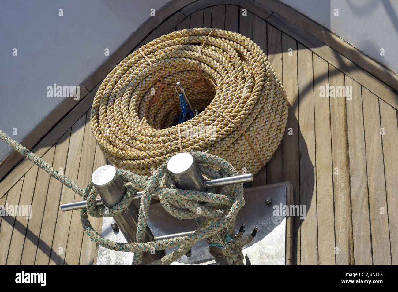 Bow of white yacht. Bay with thick rope lies on wooden deck. Rope is wound on mooring post of yacht. Top view. Close-up. Selective focus. Stock Photo