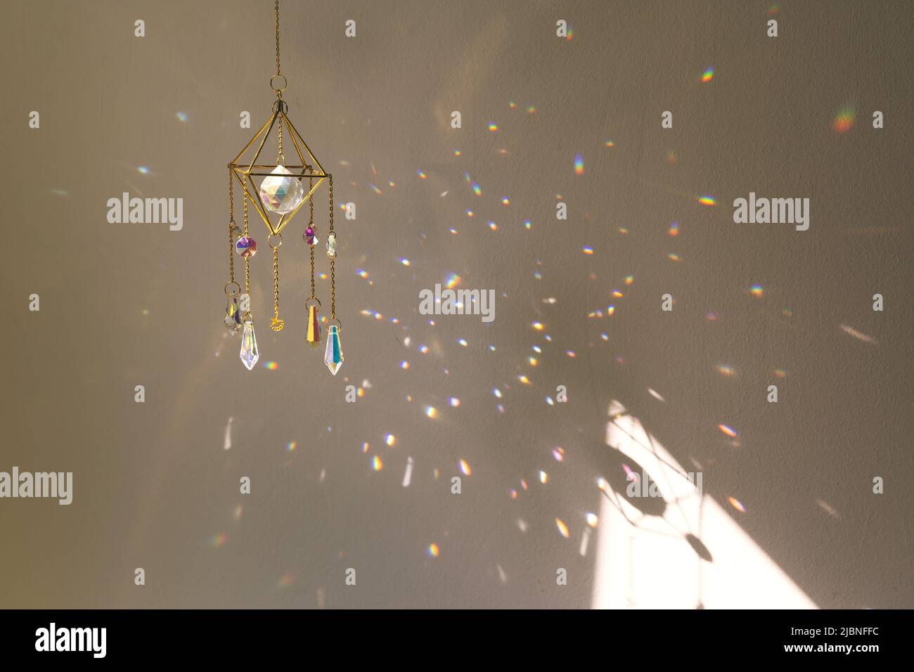 Suncatcher hanging in home during sunset. Many sun beams on the wall. Good Feng Shui, energy flow concept Stock Photo