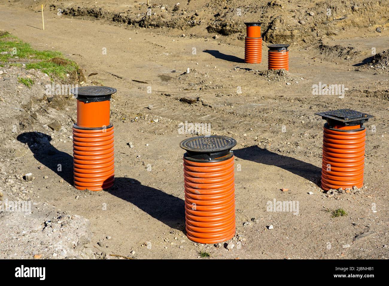 New storm water drainage wells with black iron grate cover and brown plastic sewer pipes on a new street construction site Stock Photo