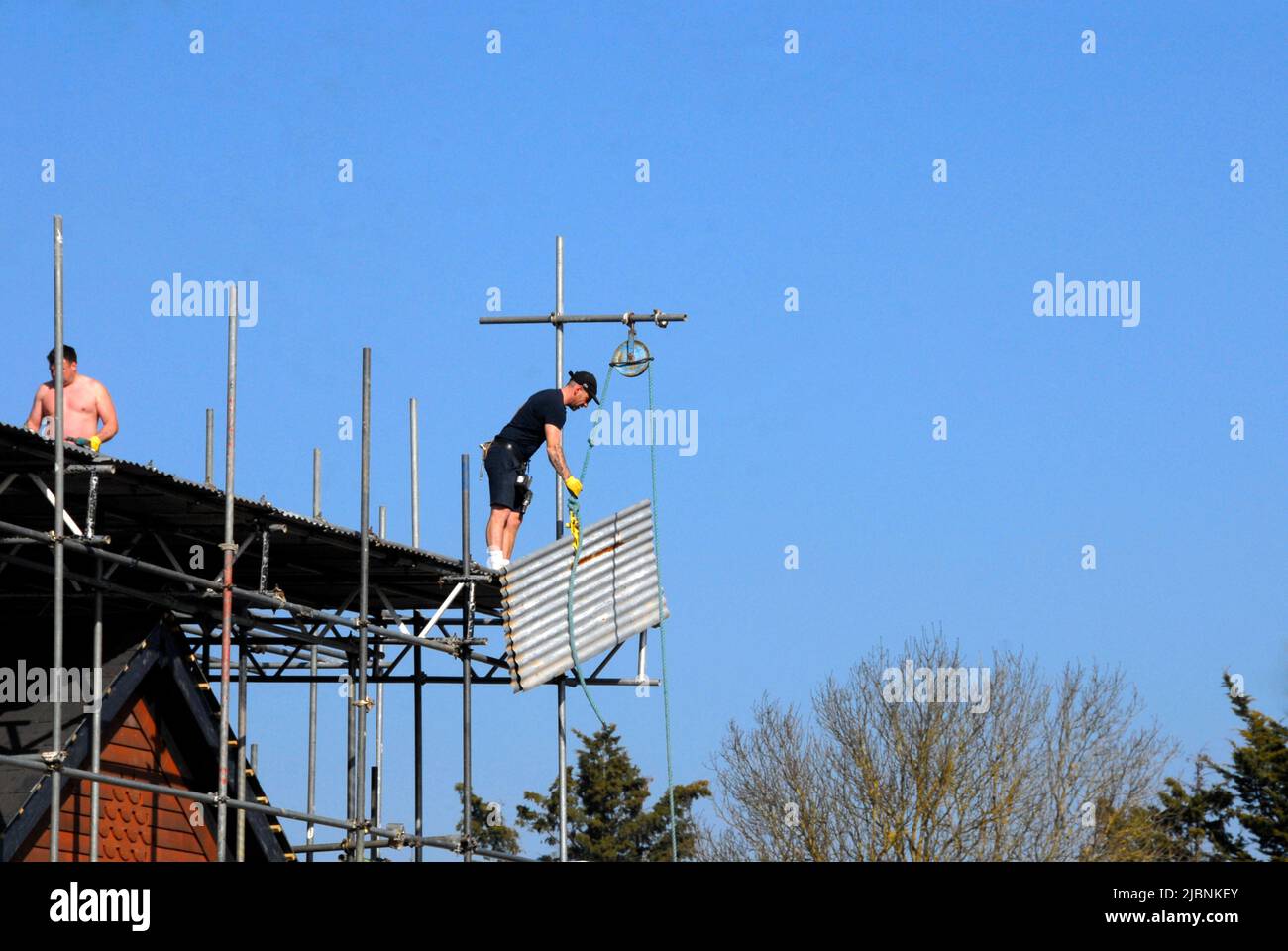 Two men removing sheets of corrugated iron from temporary roof covering on new-build house Stock Photo