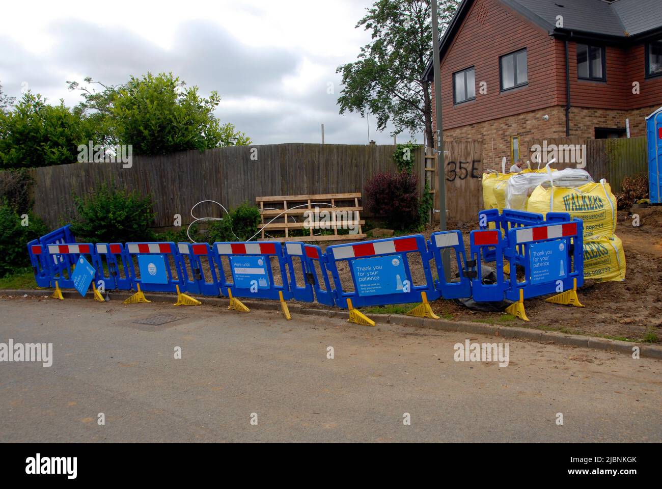 Barriers put up by water board contractors after connecting services to new house, with waste left leaning against neighboring fence Stock Photo