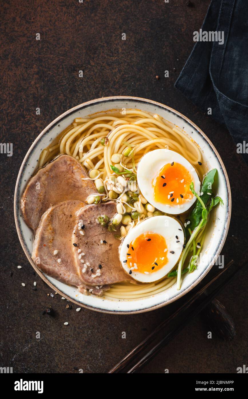 Ramen soup noodle bowl with egg and meat on dark brown background, table top view. Asian cuisine food Stock Photo
