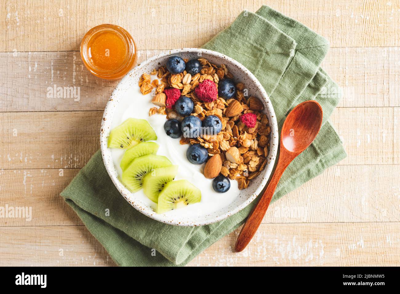 Honey nut granola yogurt bowl with blueberries and kiwi fruit on a wooden table and linen textile. Top view Stock Photo