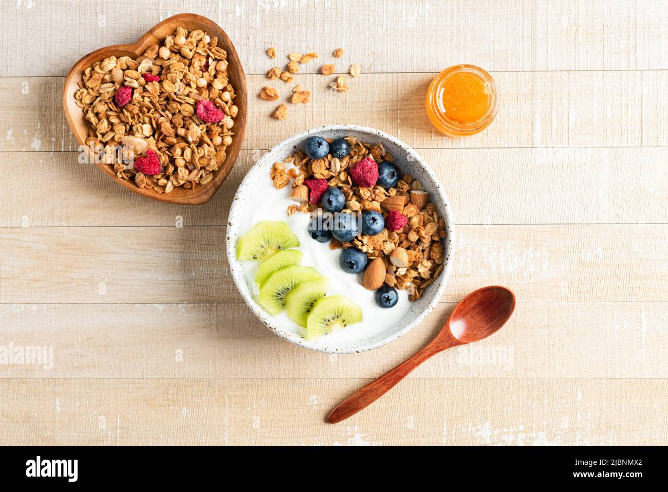 Bowl of crunchy honey granola with blueberries, kiwi and greek yogurt on a wooden background. Top view Stock Photo